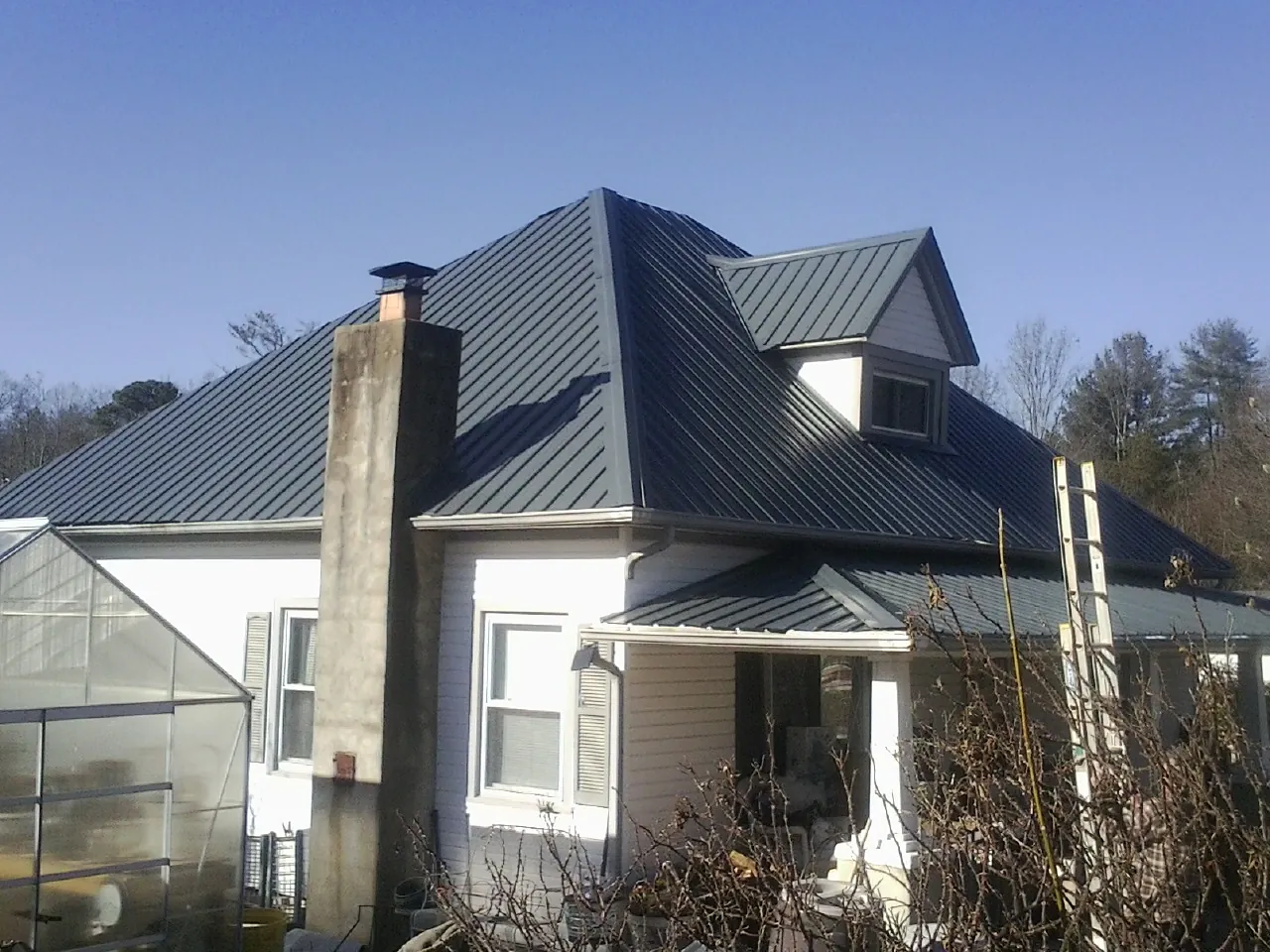 Dark blue standing seam metal roof on a white farmhouse with dormer — Slate & Tile Roof Repair by Roofing Brothers in Mount Clare