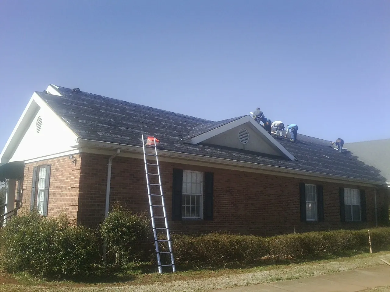 Crew tearing shingles off a brick ranch roof with a ladder set — Emergency Roof Repair work by our crew in Mount Clare