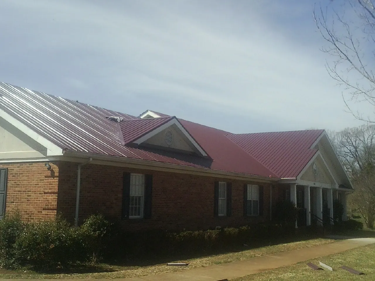 Red metal roof with gabled entries on a long brick building, from a Hail Damage Roof Repair job in Mount Clare