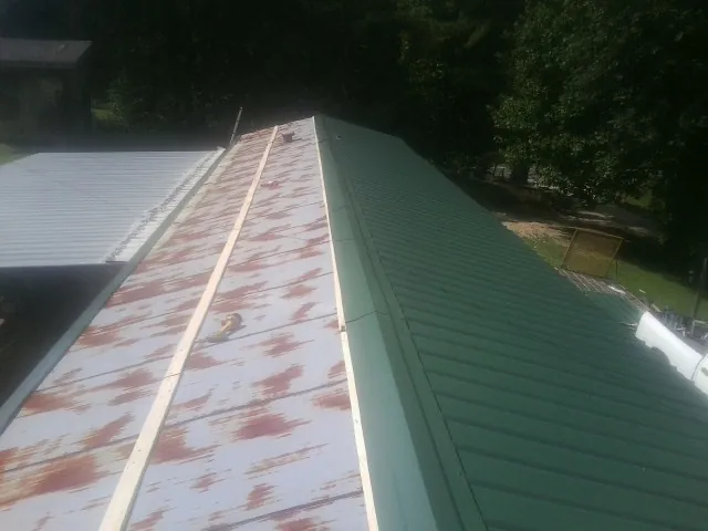 Old rusted panels beside newly installed green metal roofing — Wind Damage Roof Repair by Roofing Brothers in Mount Clare