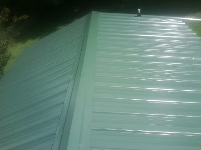 New green metal panels meeting at the ridge of a roof — Flat Roof Repair work by our crew in Mount Clare